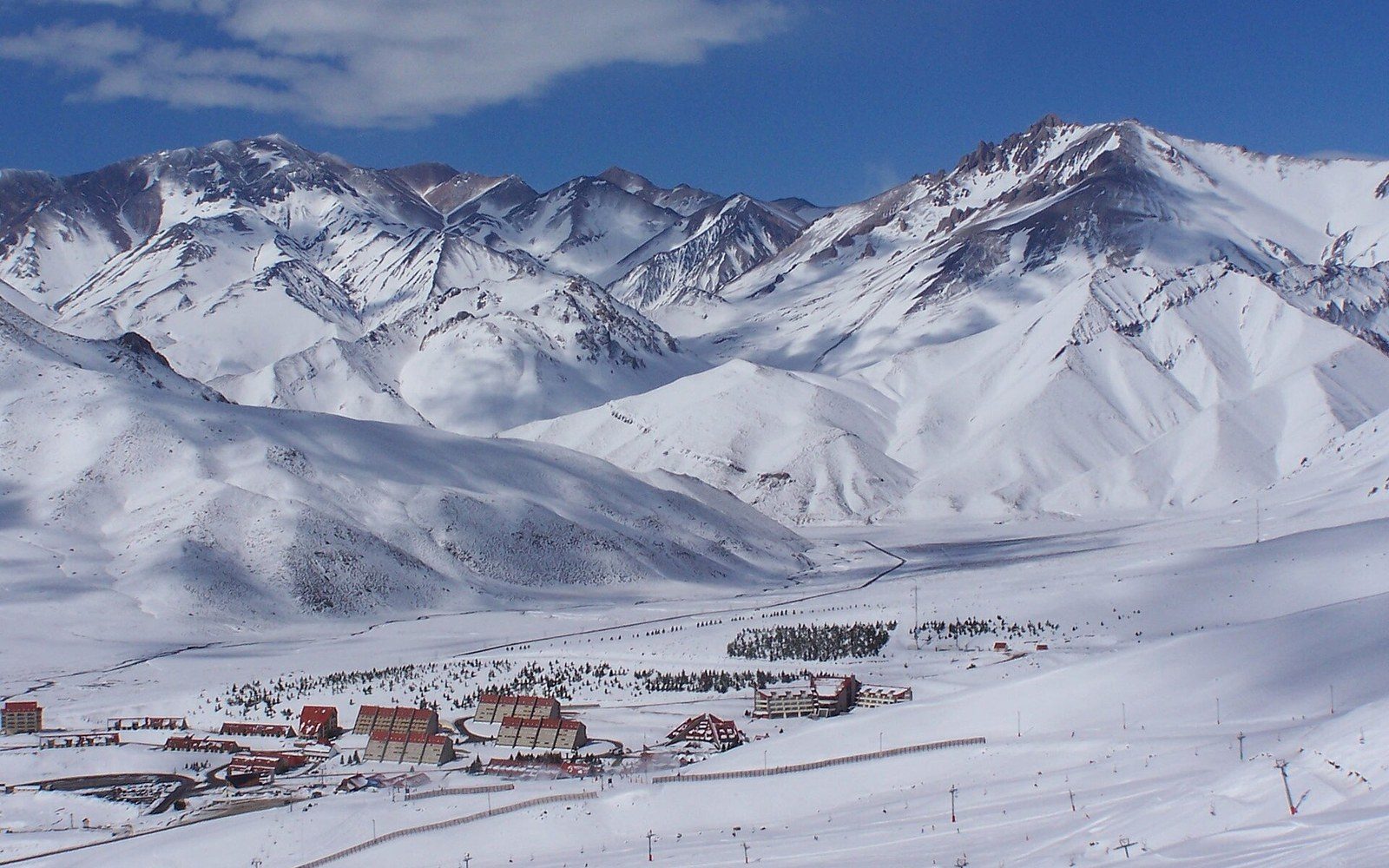 Snow-covered mountains surround the Las Leñas resort buildings in a wide valley